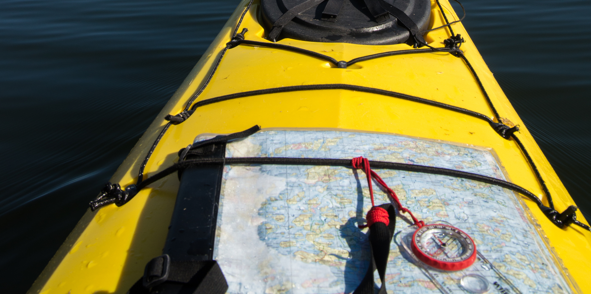 Map and compass under bungees on a yellow sea kayak