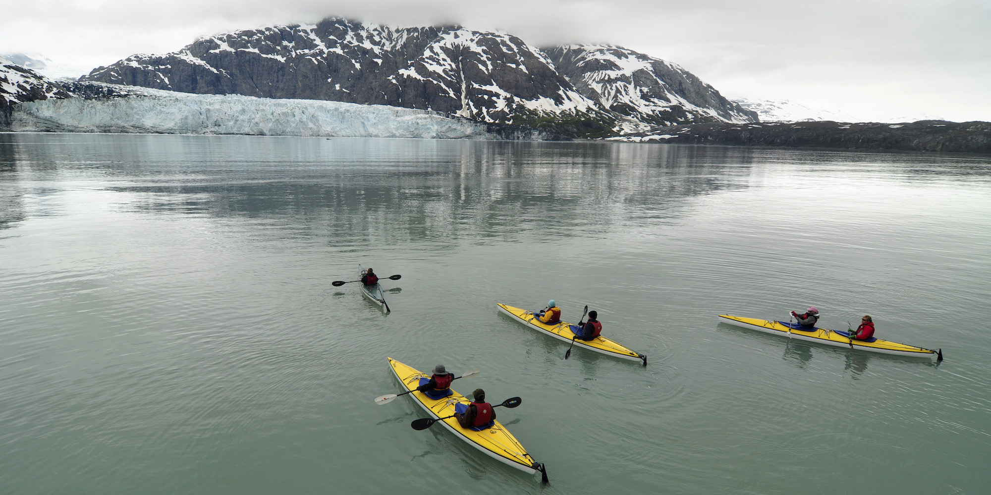 People in yellow tandem sea kayaks paddling through the Kenai Fjords in Alaska