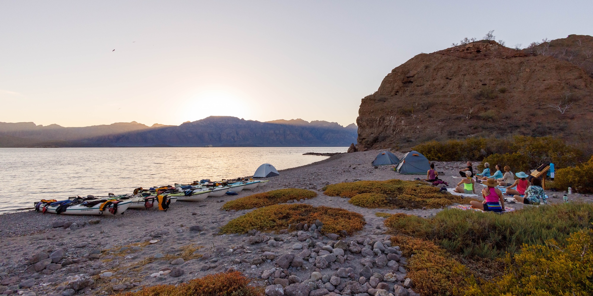 A group of sea kayakers lounging on the beach during a sunset in Baja, Mexico.