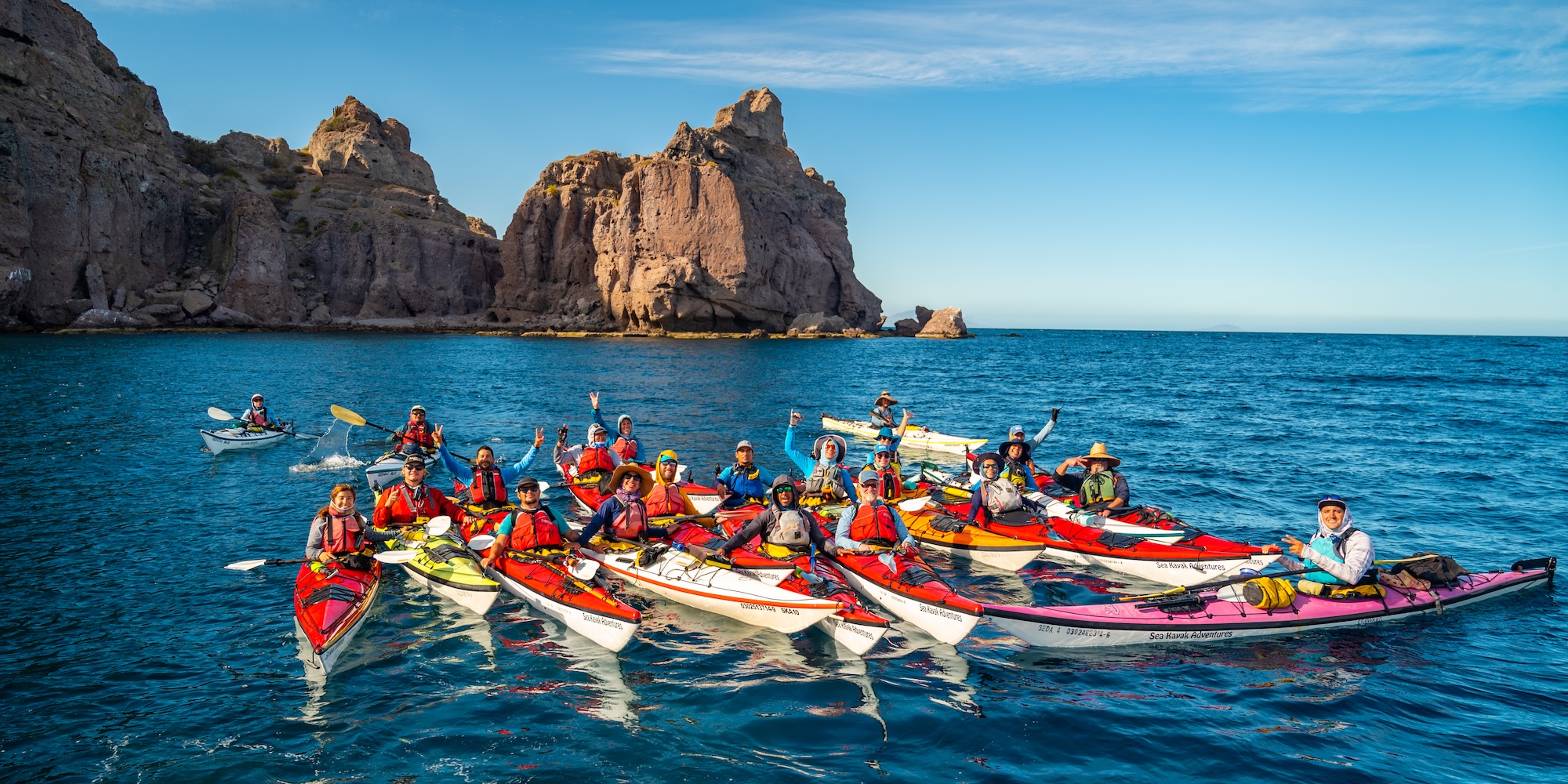 Group of smiling kayakers floating together near dramatic rock formations in the Sea of Cortez during a guided Baja sea kayaking tour.